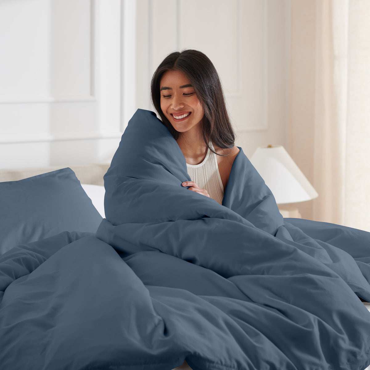 Woman smiling under duvet cover set in a bedroom setting