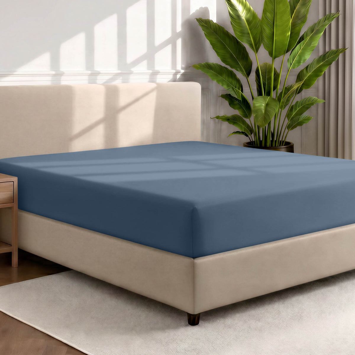 Bed with a fitted sheet in a room with a large plant and rug