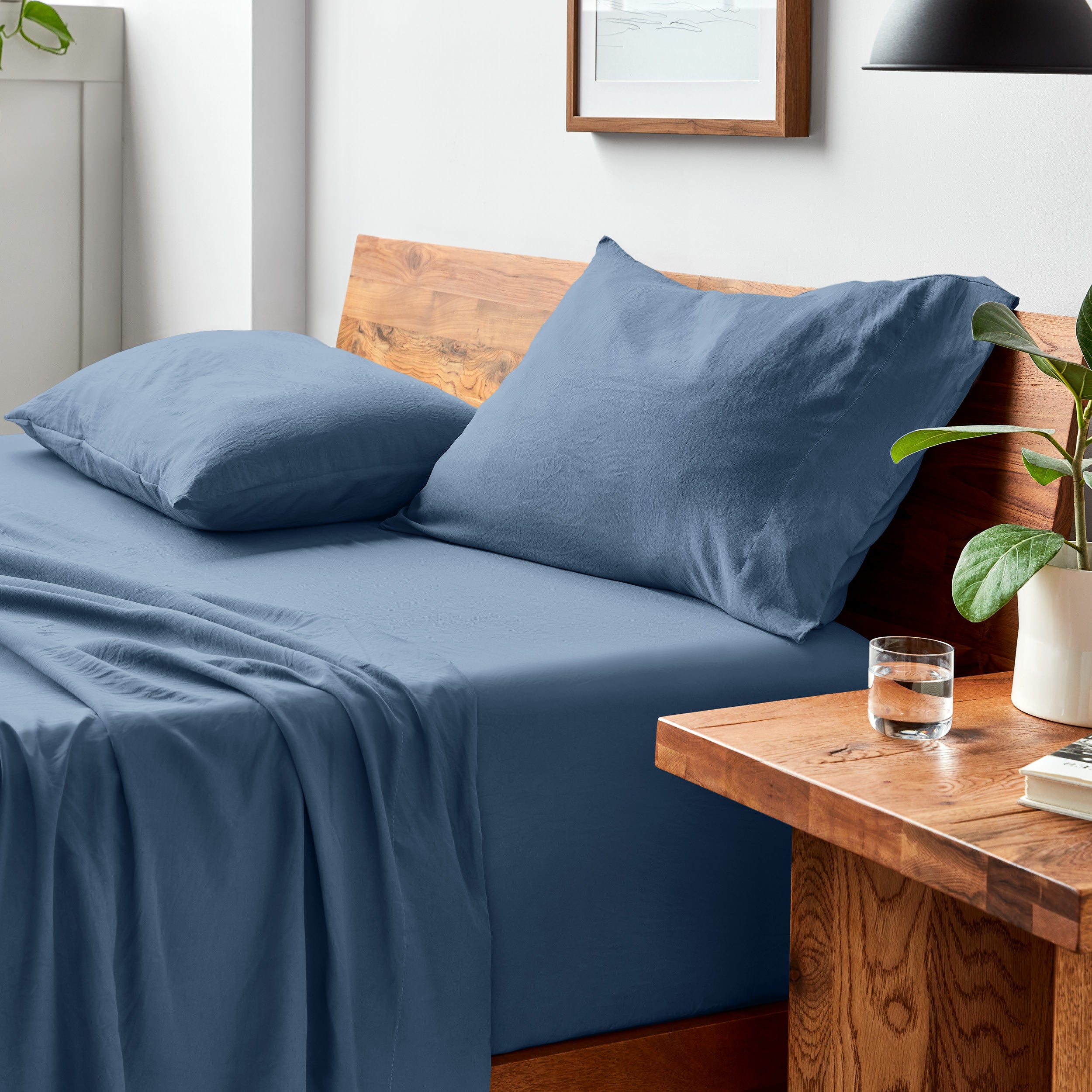 Washed bed sheets on a bed with a wooden headboard and side table