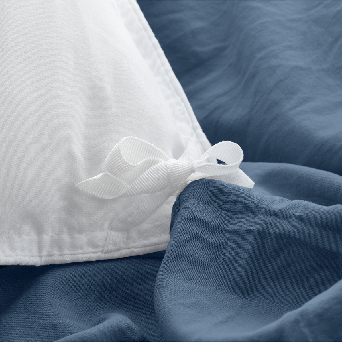 Bed with washed bedding and white pillows in a bright room
