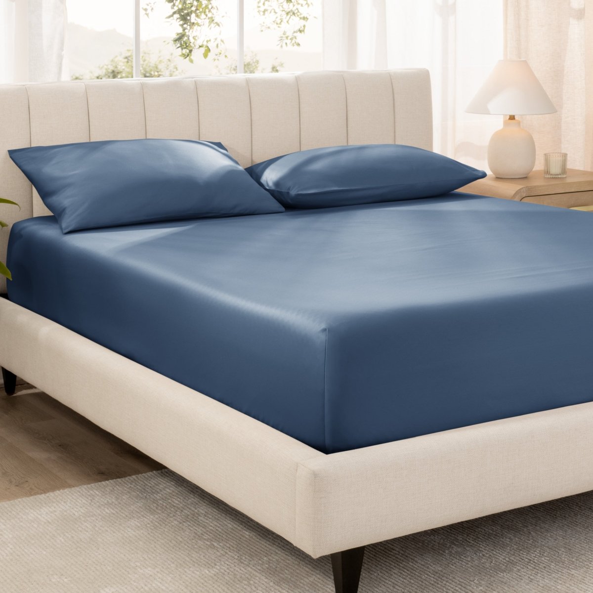 Bed with fitted sheet and pillowcases in a bright room.