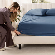Woman adjusting a fitted sheet on a bed in a bedroom setting