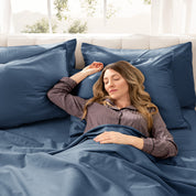 Woman lying in bed with sateen bedding and pillowcases, looking relaxed.