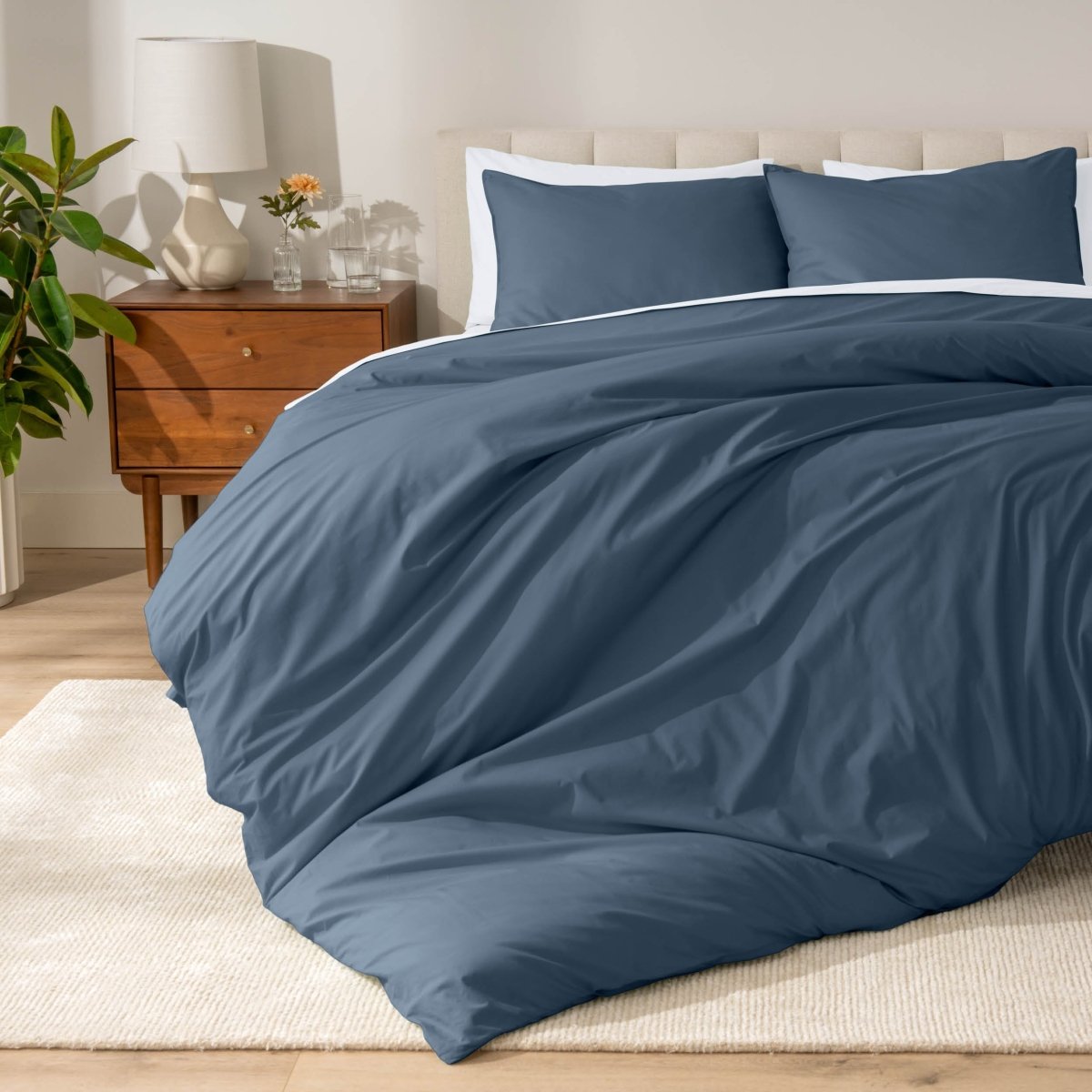 Percale bedding set on a bed in a bedroom with a wooden nightstand and lamp.