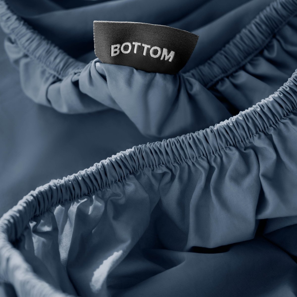 Close-up of a fitted sheet with a black fabric brand label reading BOTTOM.