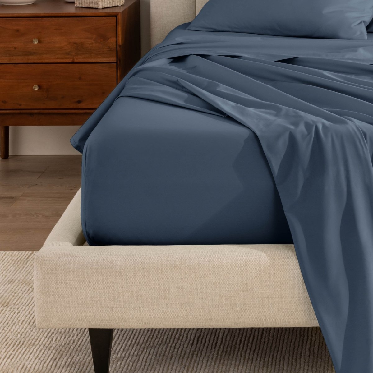 Top sheet and a matching fitted sheet on a bed with a beige bed frame