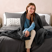 A woman sitting on a bed with a Sherpa blanket around her