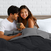 Man and woman sitting on a bed holding a mug, smiling at each other.