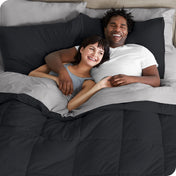 A couple is lying in bed with a comforter and sheets over them