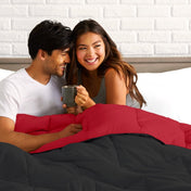 Man and woman sitting on a bed holding a mug, smiling at each other.