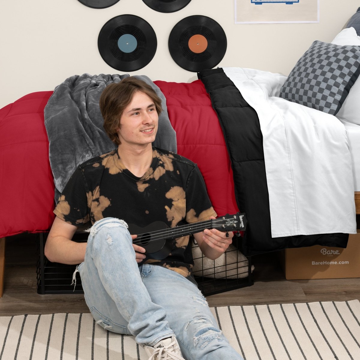 Person sitting on a bed holding a guitar in a bedroom setting with vinyl records on the wall.