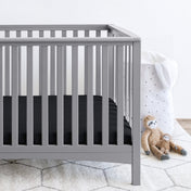 Gray crib with stuffed animals on the floor next to it