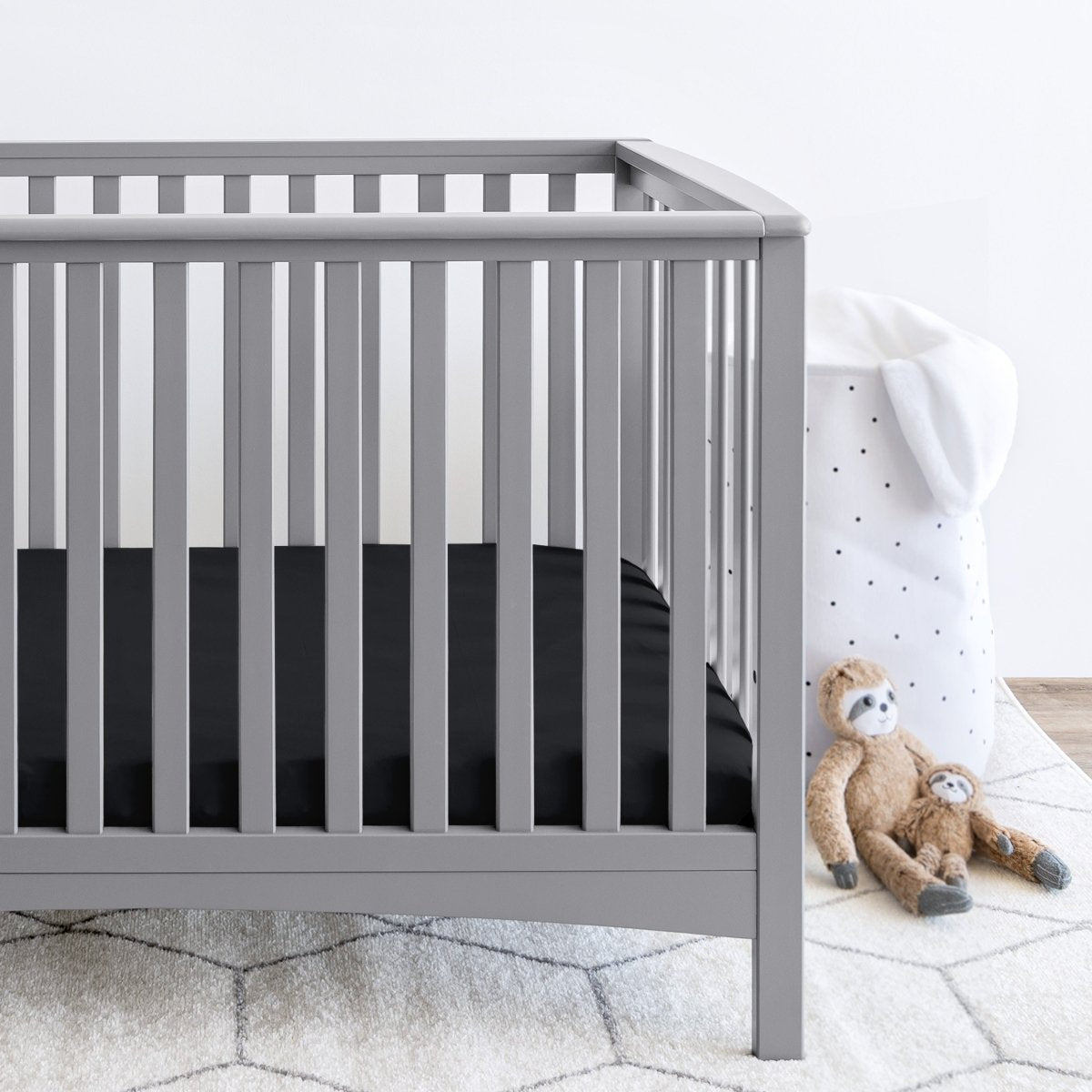 Gray crib with stuffed animals on the floor next to it