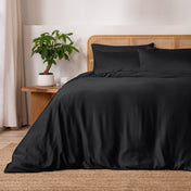 Black bedding set on a bed with a wicker headboard and plant in the background.