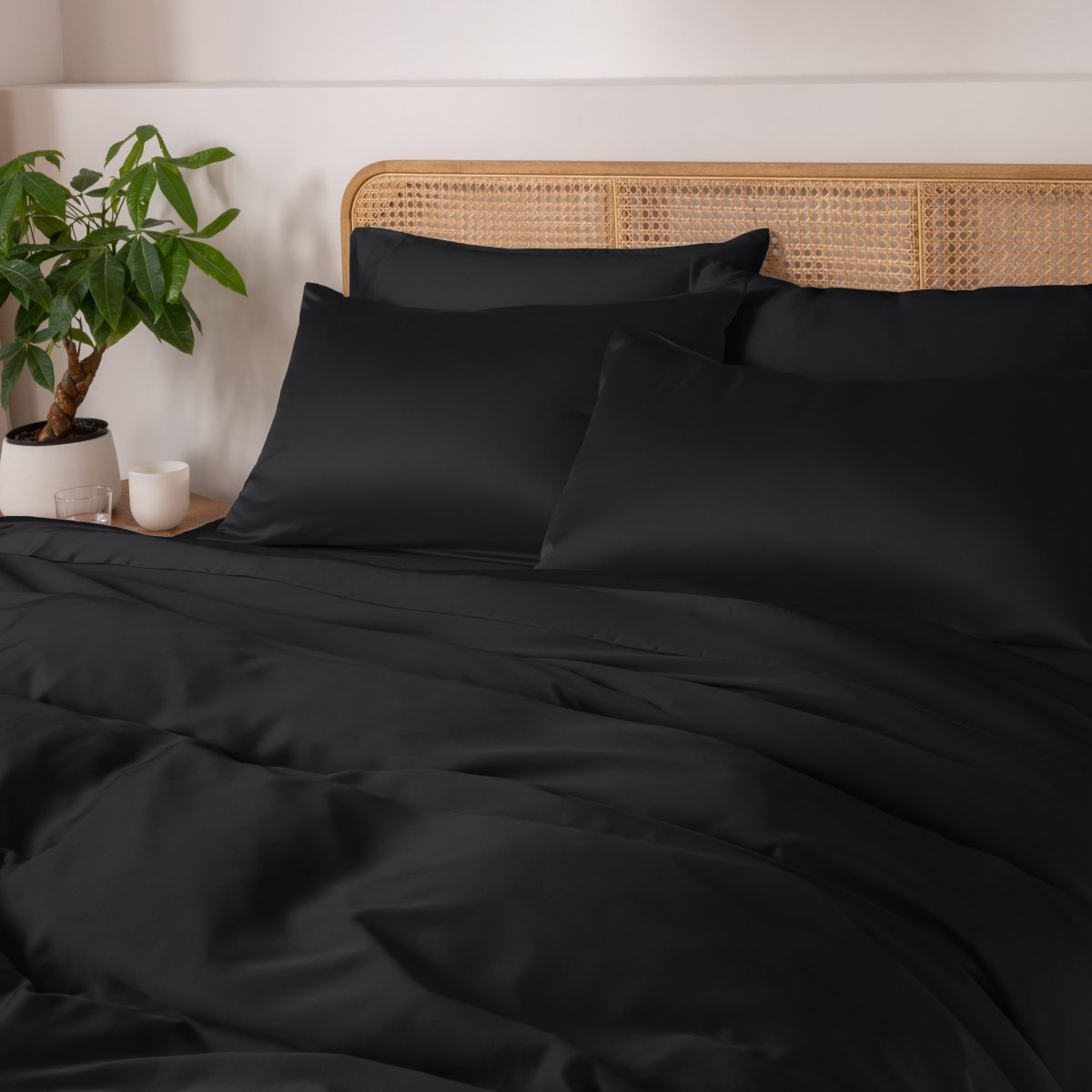 Black bedding set on a bed with a wicker headboard and plant in the background