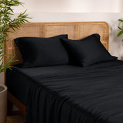 Bamboo bed sheets and pillows on a bed with a wicker headboard in a room with plants.
