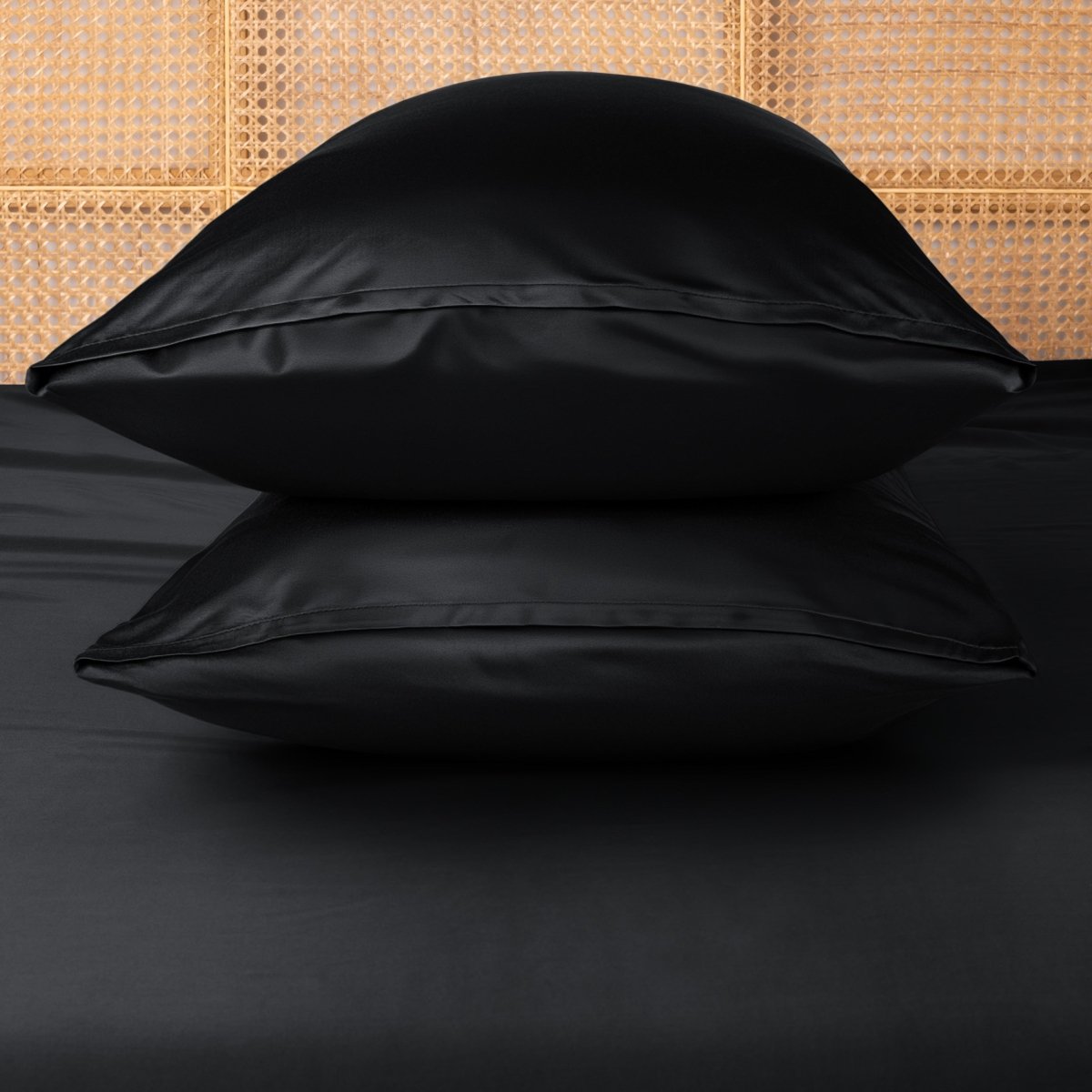 Two black pillows stacked on a bed with a woven headboard.