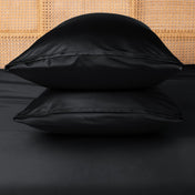 Two black pillows stacked on a bed with a woven headboard.