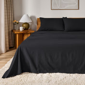 A bed dressed in flannel sheet set in a bedroom with a wooden headboard, bedside table and lamp