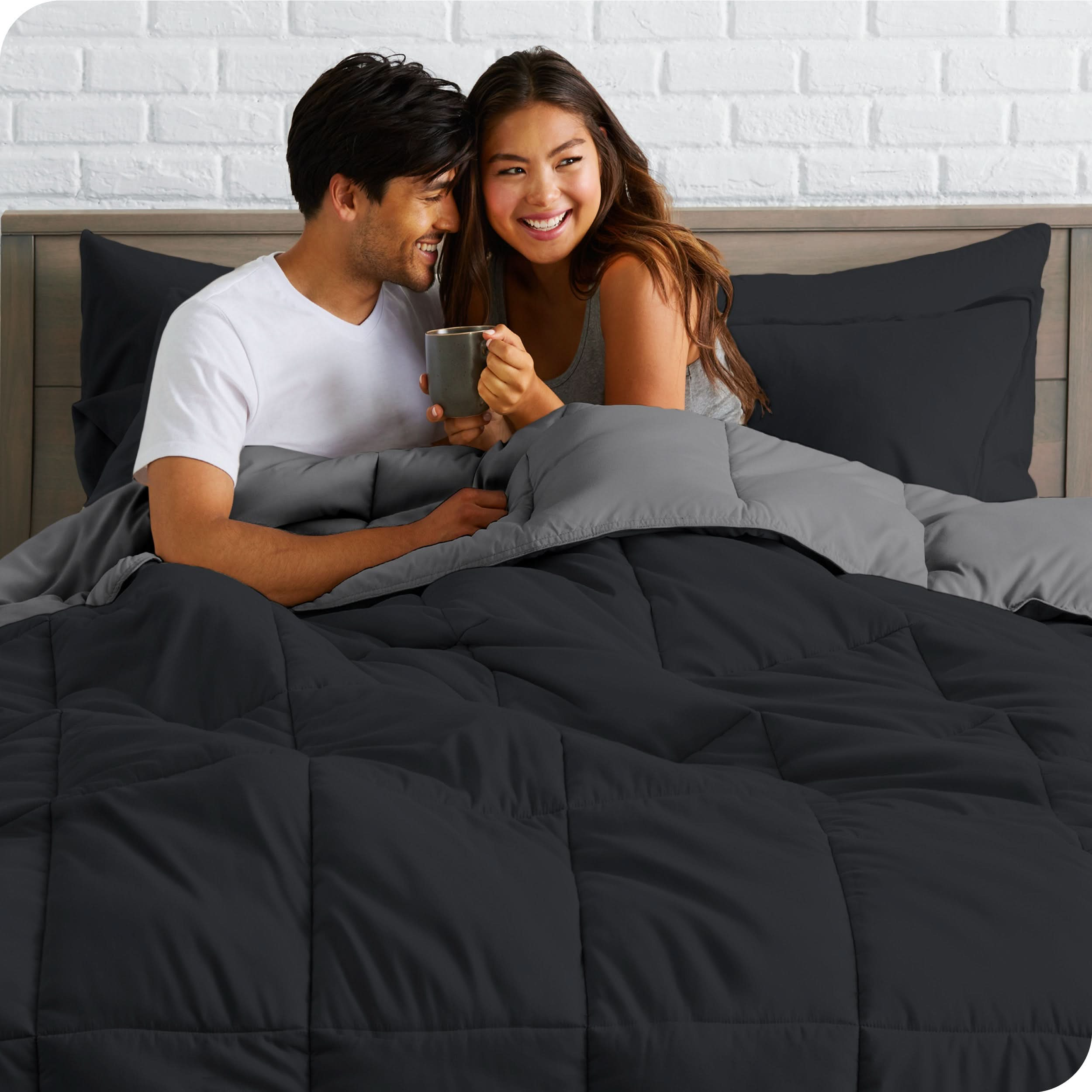 A couple sitting in a bed made with a reversible comforter and sheet set