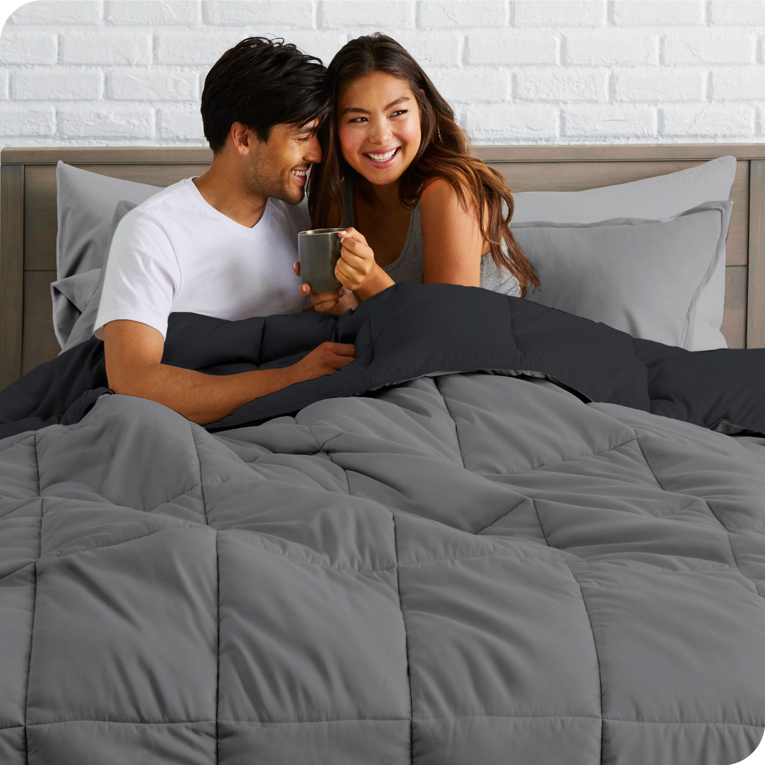 A couple sitting in a bed made with a reversible comforter and sheet set