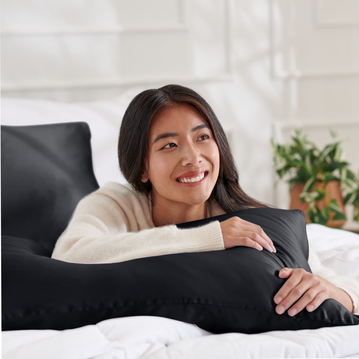 Woman lying on a bed with a body pillow, smiling.
