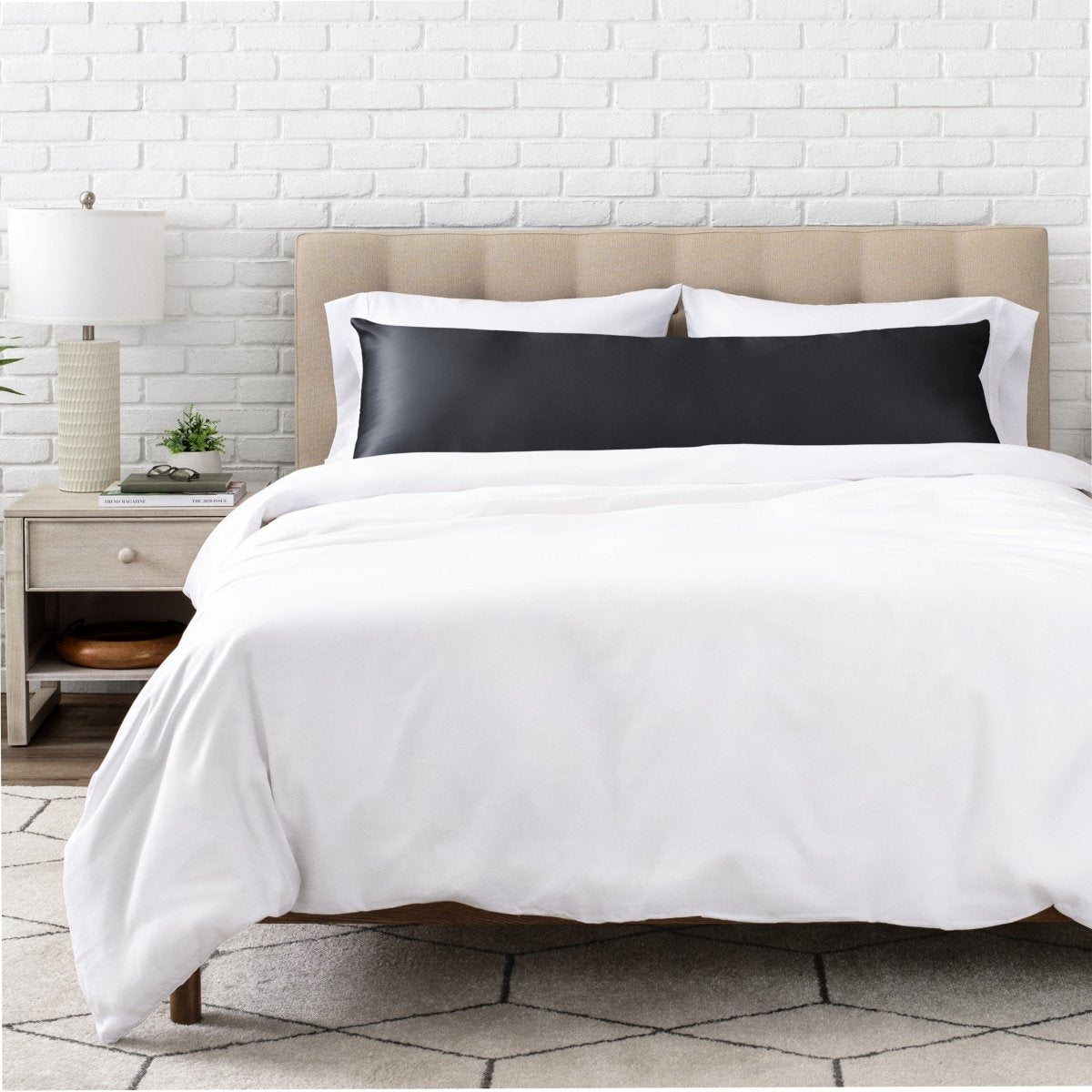 Bed with white bedding and satin pillowcase against a white brick wall.
