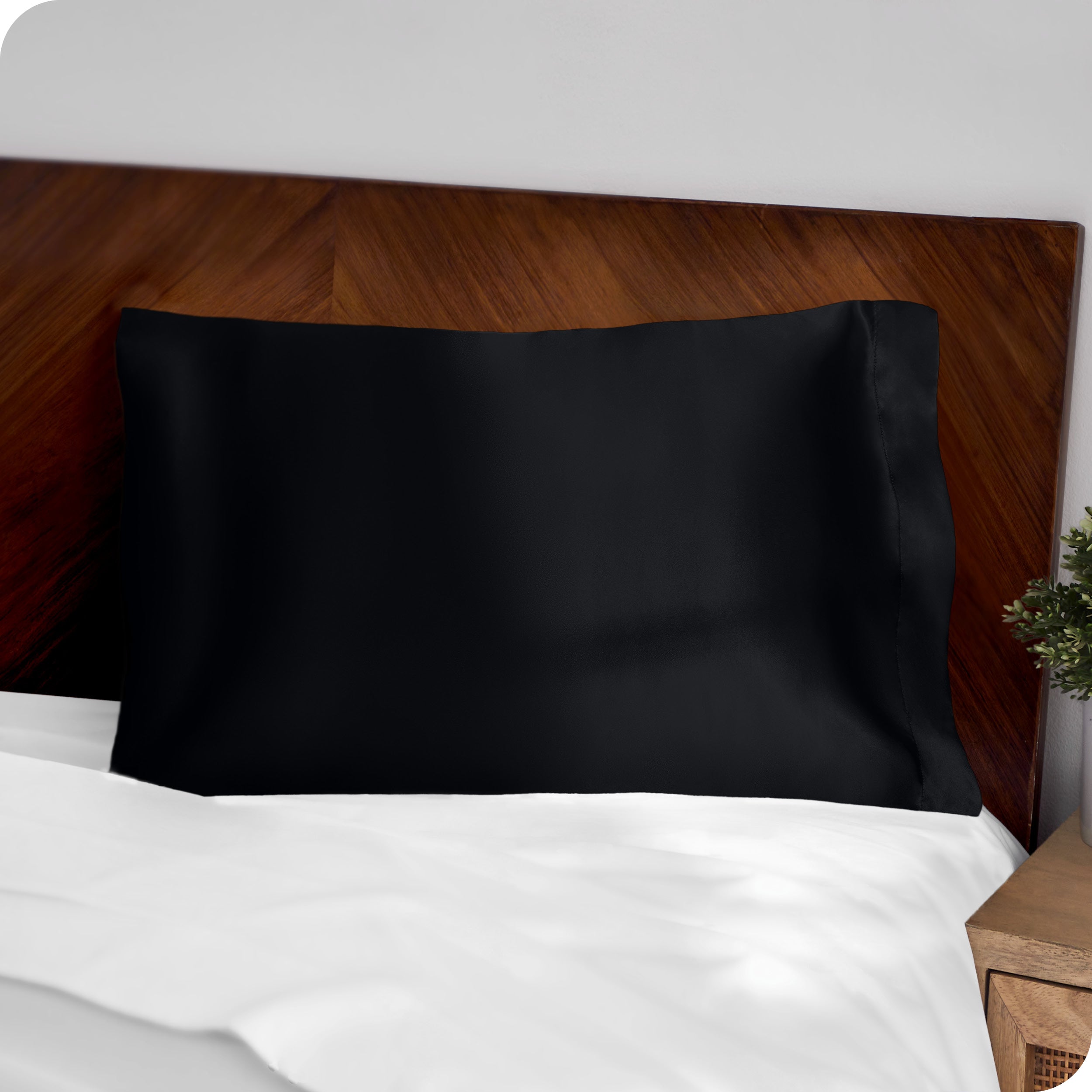 A black silk pillowcase on a pillow resting on a headboard