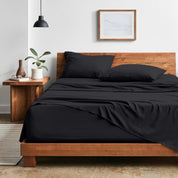 Bedroom with sheet set on a wooden bed frame, side table with plant and lamp.