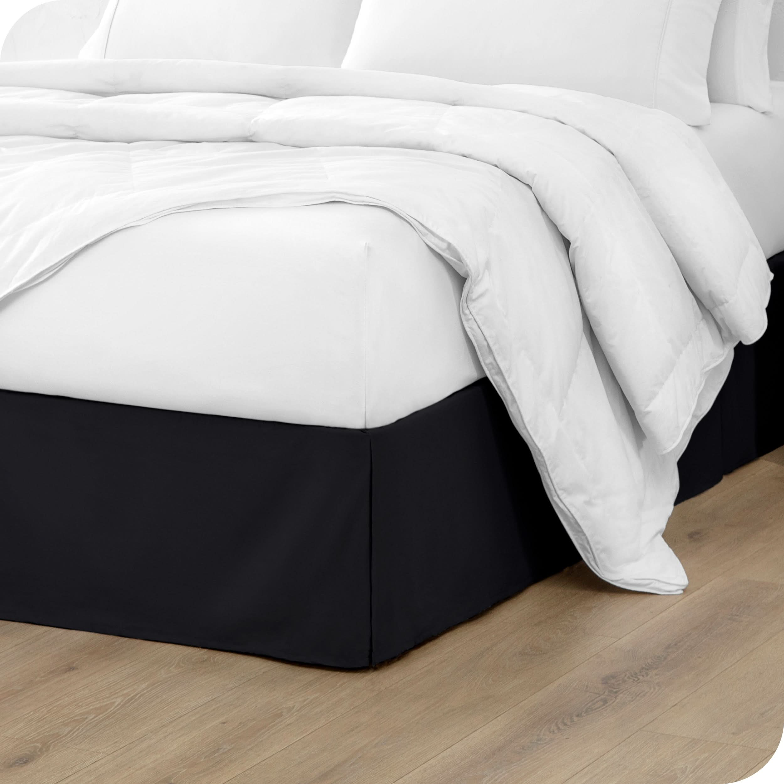 A modern bed with a microfiber bed skirt with pleats on the corners and midway on each side.