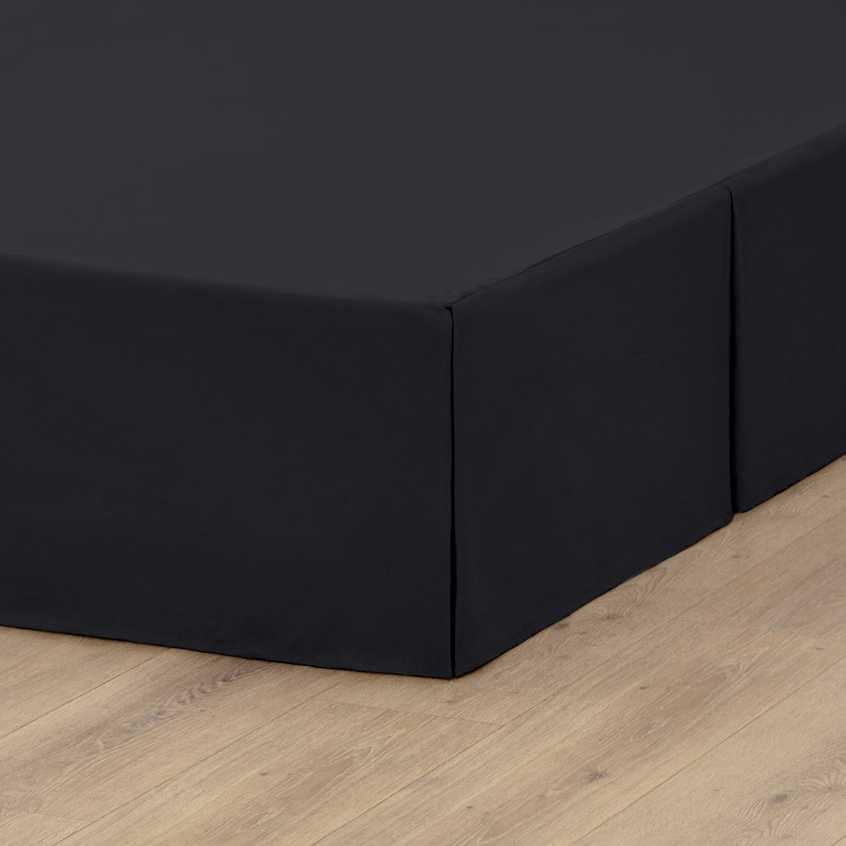 The corner of a box spring with a pleated bed skirt on it