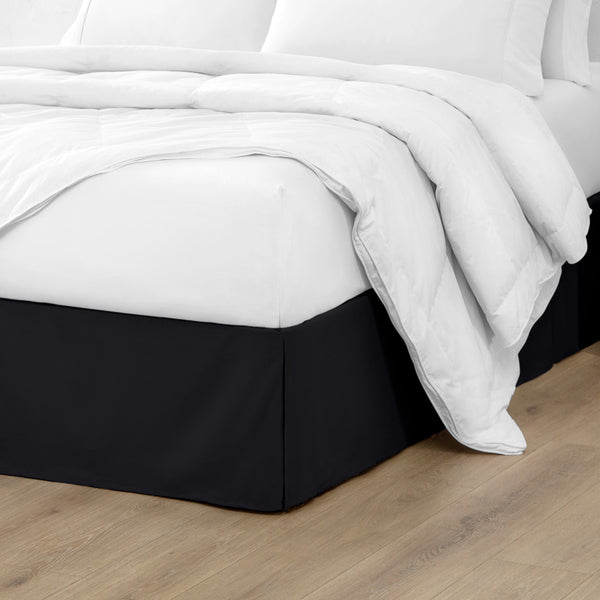 A modern bed with a microfiber bed skirt with pleats on the corners and midway on each side