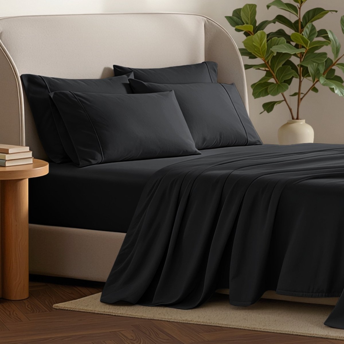Bed sheets and pillows on a bed with a plant and side table in the background.
