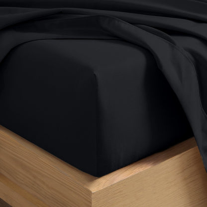 A close-up of a fitted sheet covering the corner of a bed frame, with matching top sheet draped over it.