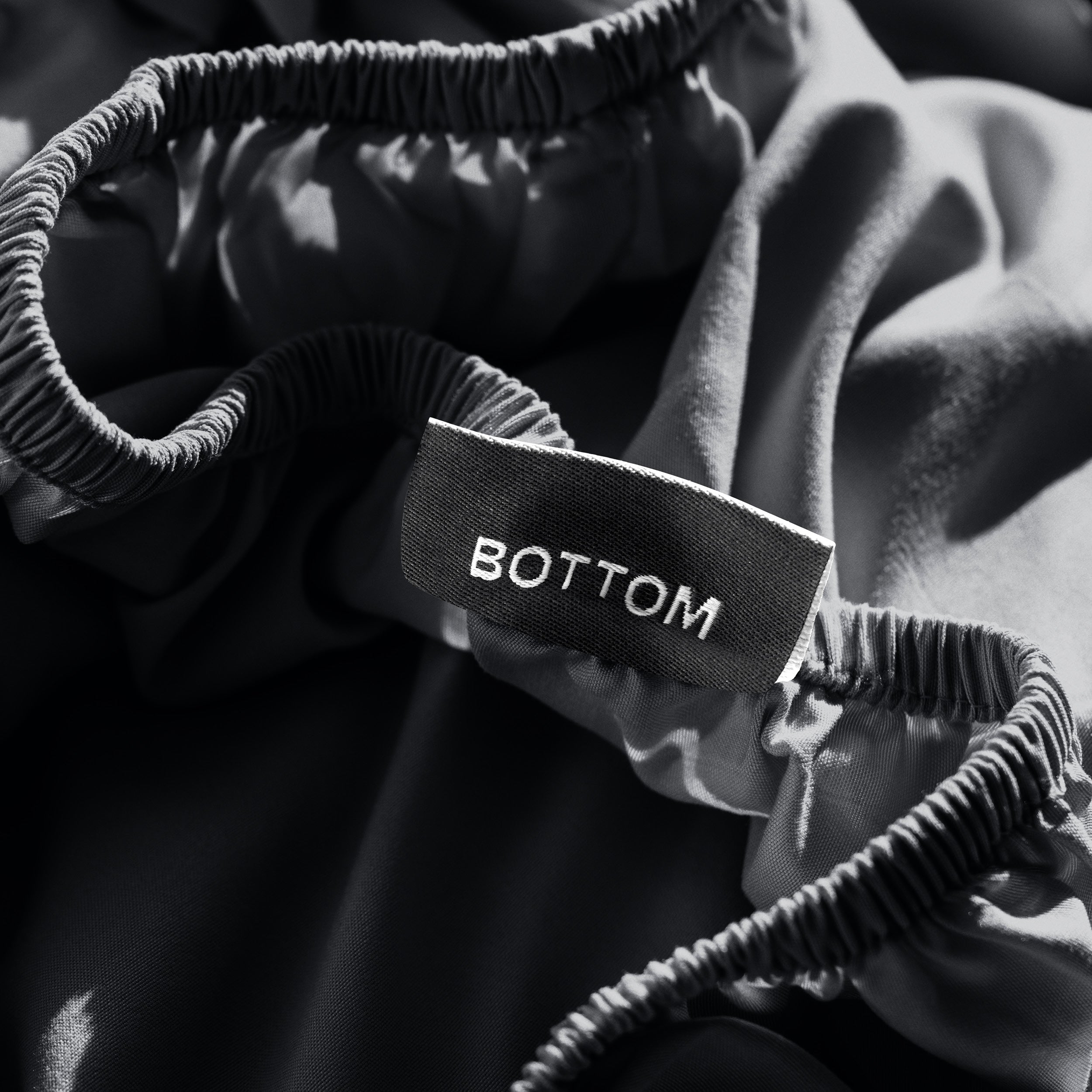 A close-up of a fitted sheet with a label printed with the word 'BOTTOM' in white.