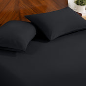 Fitted sheet and pillowcase set on a bed with a dark wood headboard and a small potted plant in the background.