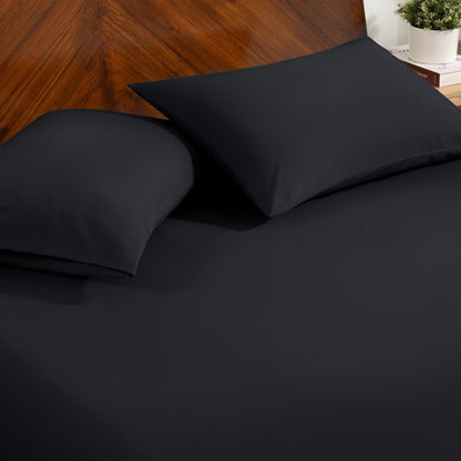 Fitted sheet and pillowcase set on a bed with a dark wood headboard and a small potted plant in the background.