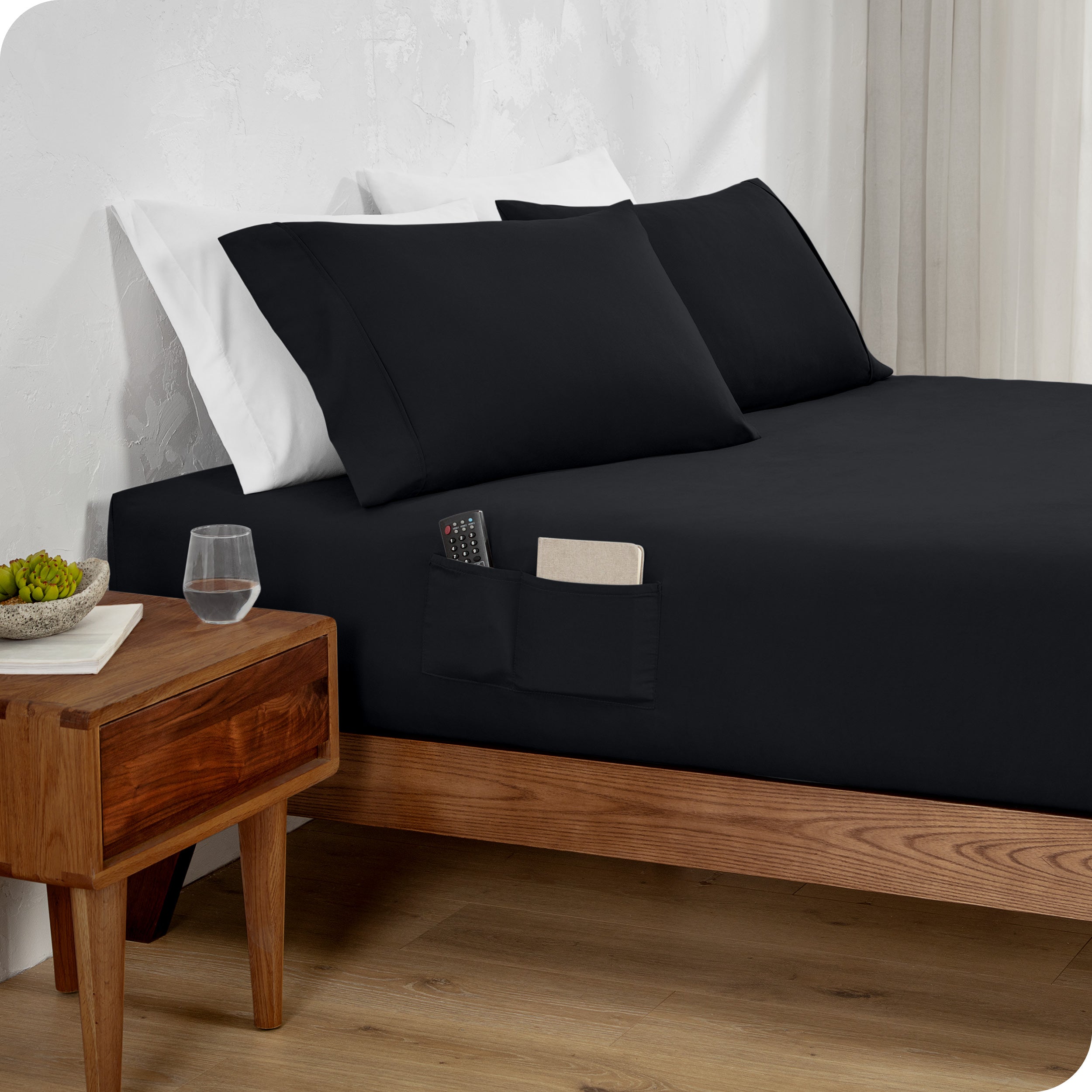 Bed made with a black fitted sheet which has pockets on the side