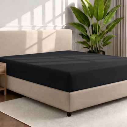 Bed with a fitted sheet in a room with a large plant and rug