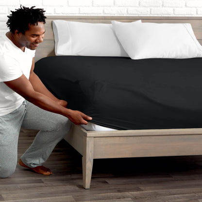 Man adjusting fitted sheet on a bed with white pillows.