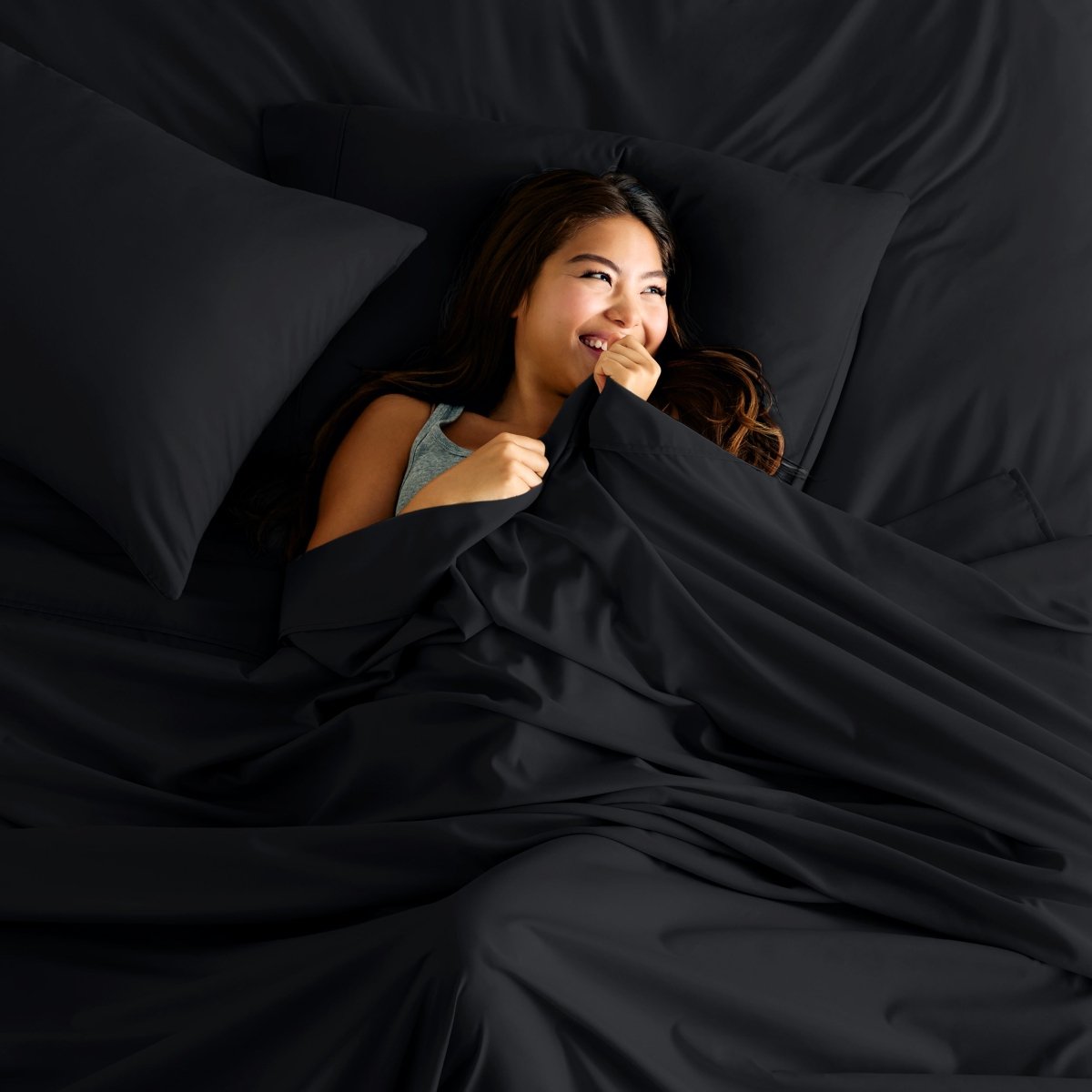 Woman lying in bed under a sheet smiling.