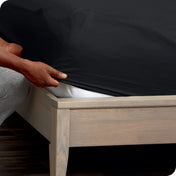 A man is putting a fitted sheet on a mattress