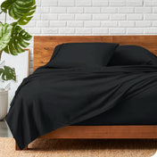 A wooden bed frame with a microfiber sheet set on the mattress.