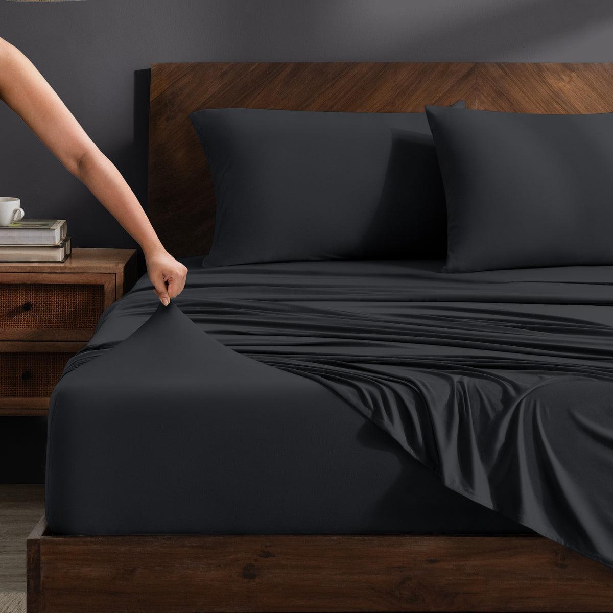 Person adjusting stretch sheets on a bed with a wooden headboard.