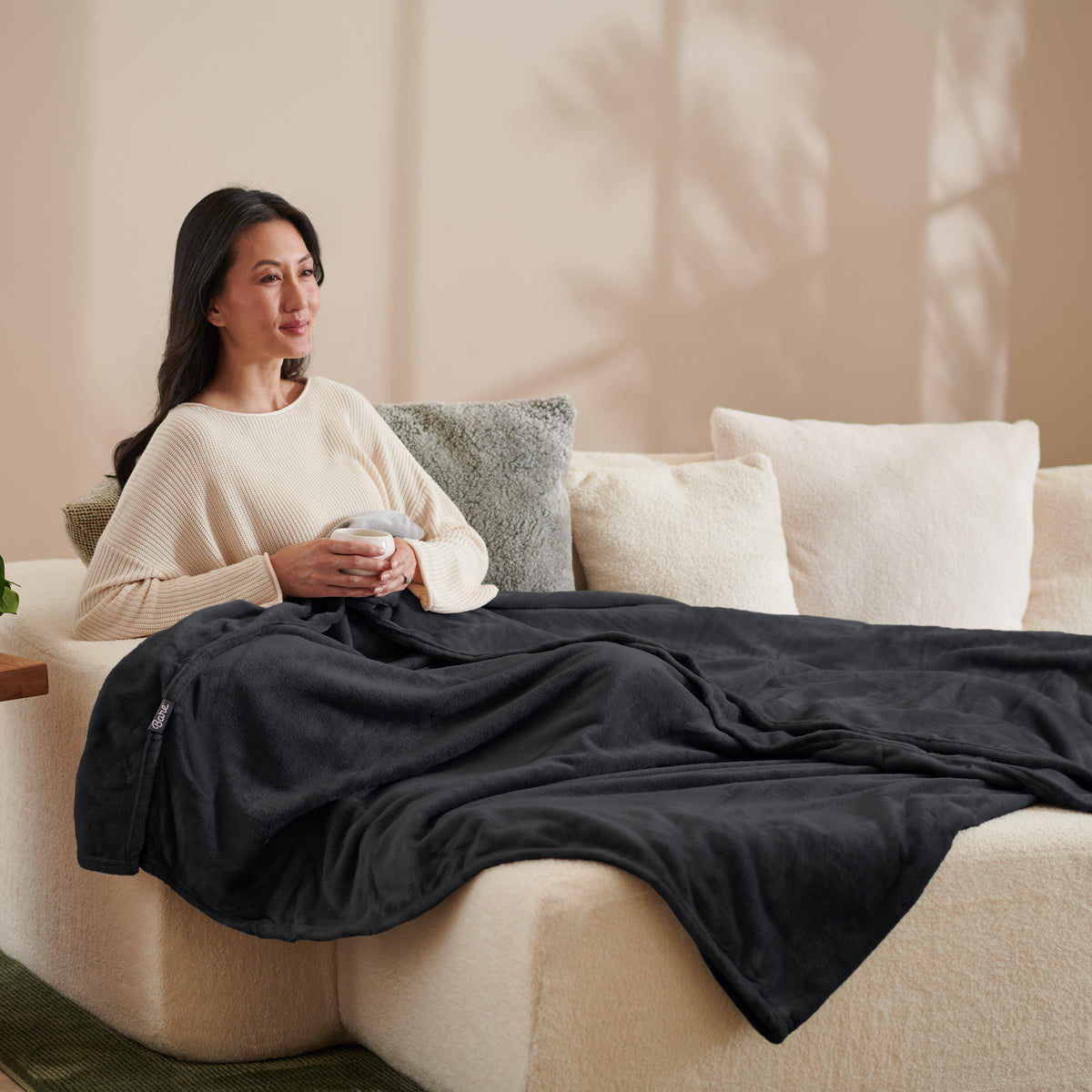 A woman sitting on a couch with a microplush blanket on her lap
