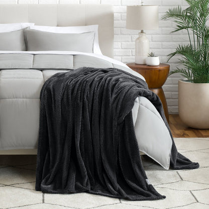 Blanket draped over a bed in a bedroom setting with a lamp and plant.