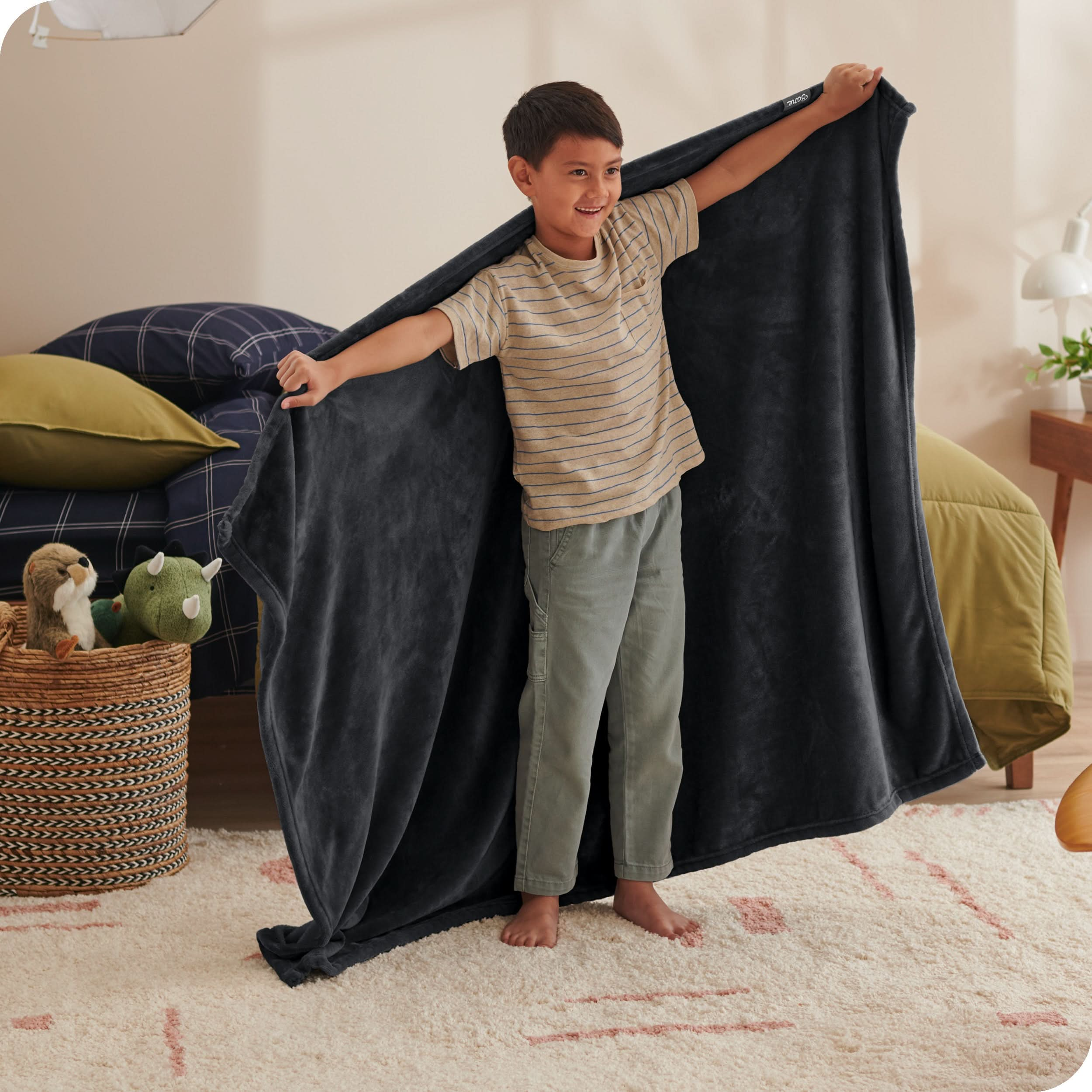 A child has his arms stretched out while holding a microplush blanket behind him