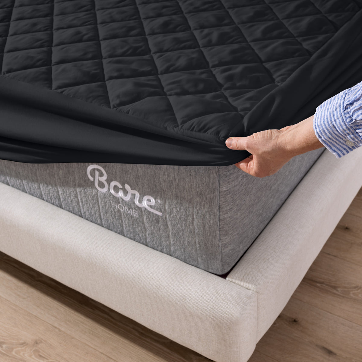 Person putting a mattress cover over a Bare Home branded mattress on a wooden floor.