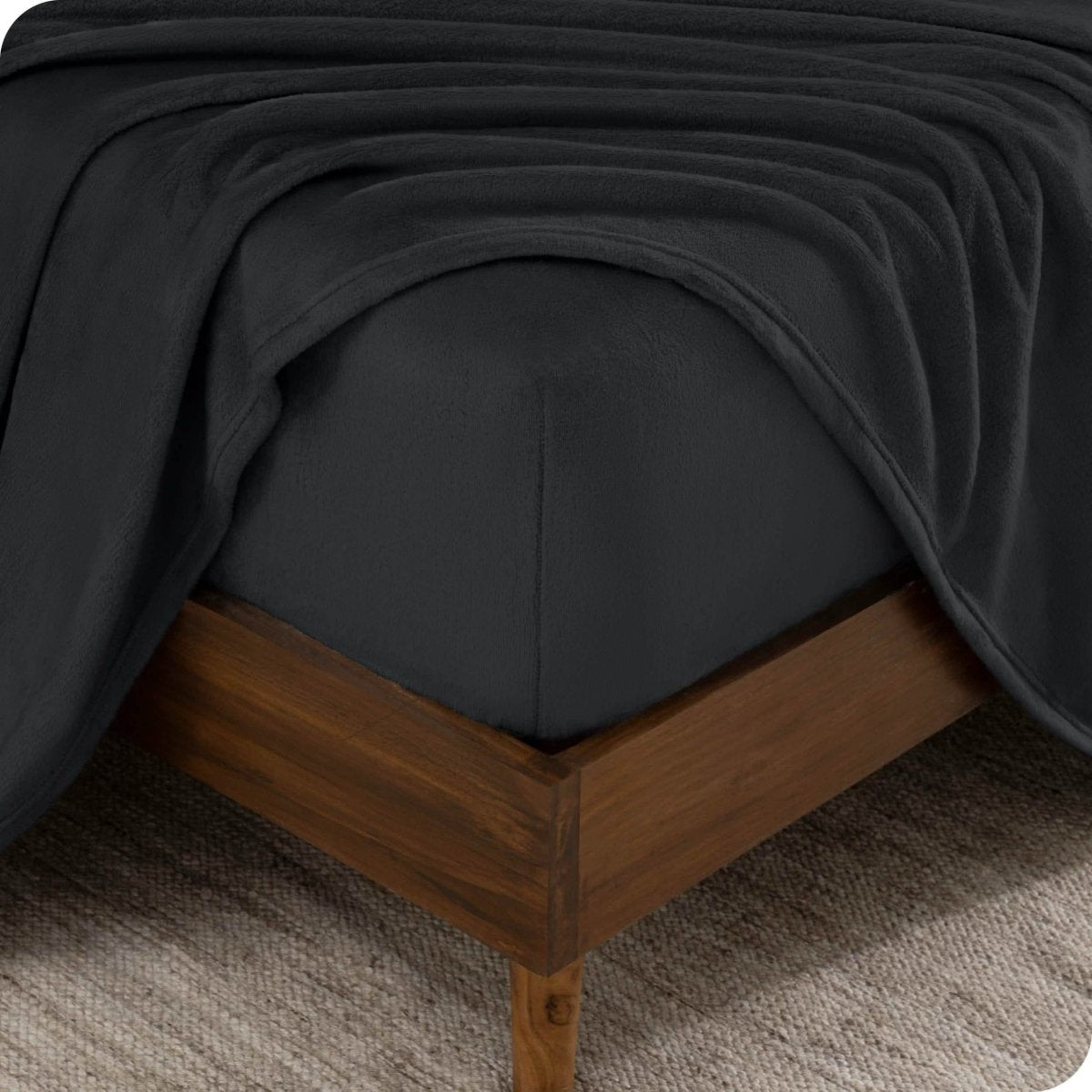The corner of a bed frame and mattress with a fitted sheet and flat sheet on it.