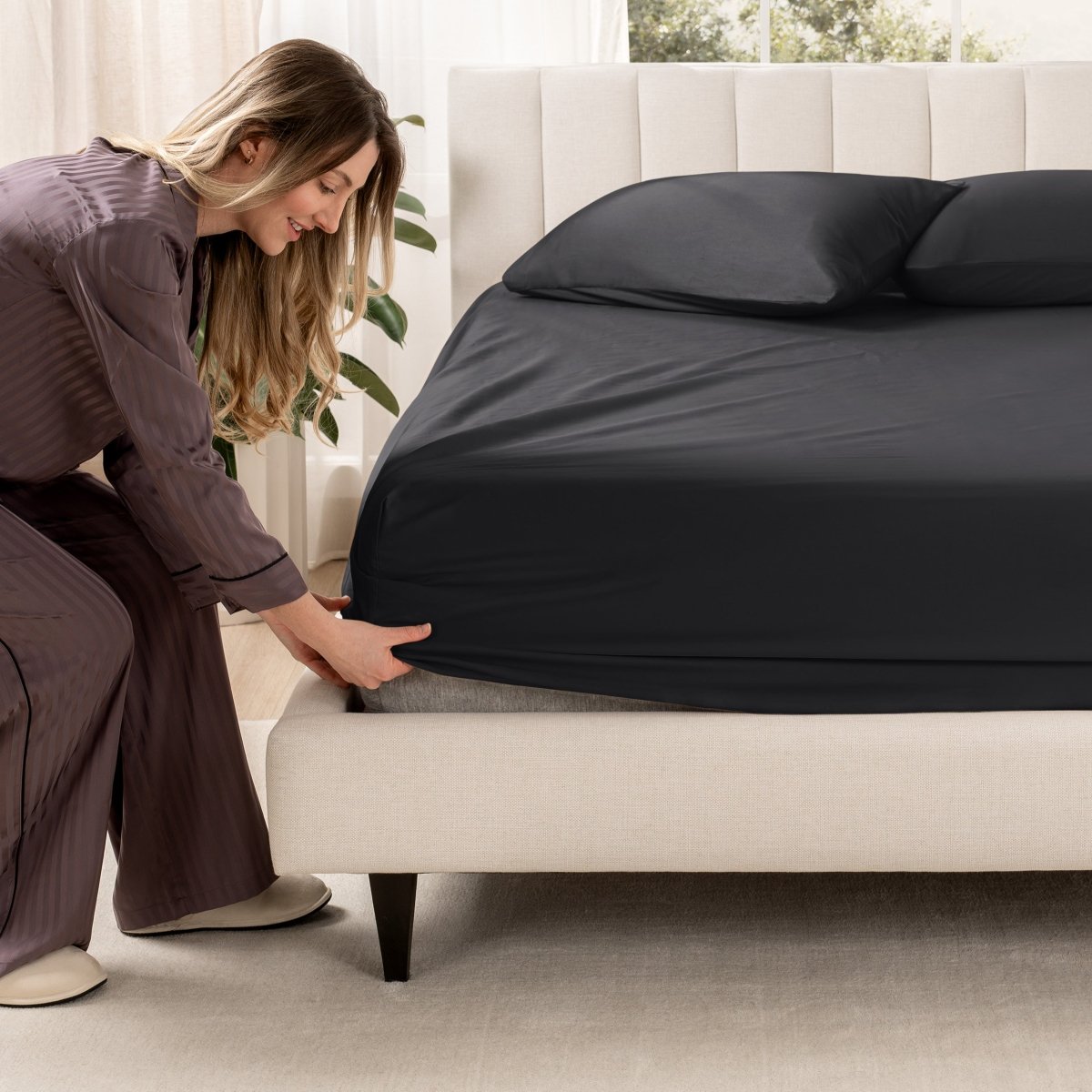 Woman adjusting a fitted sheet on a bed in a bedroom setting